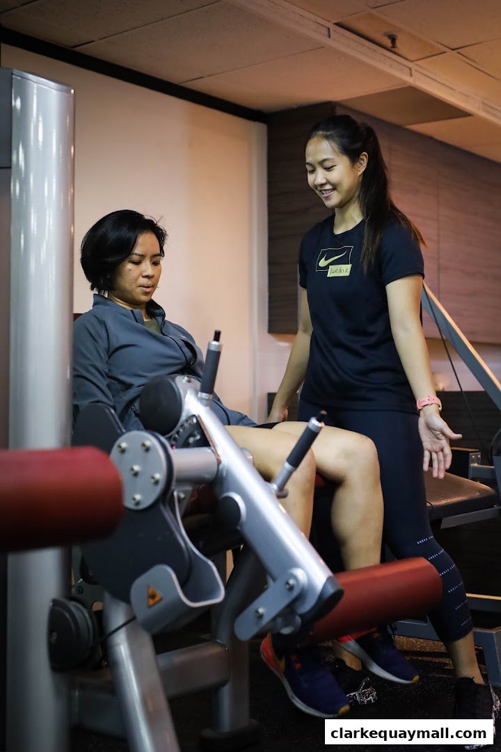 A trainer assists a client on a leg press machine at JG FIT.