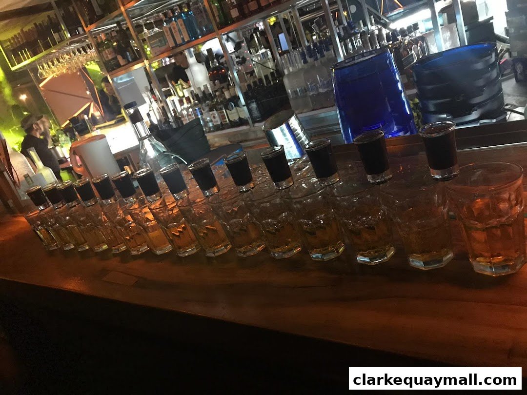 A bar counter with multiple rows of shot glasses and tumblers filled with amber liquid.