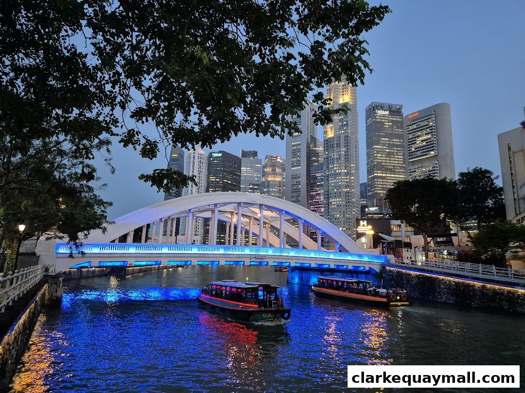 Singapore River Cruise boats pass under a bridge with city skyline at dusk.