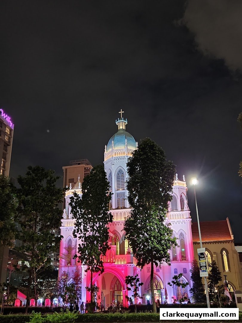 A grand building illuminated with pink and white lights at night, with trees in the foreground.
