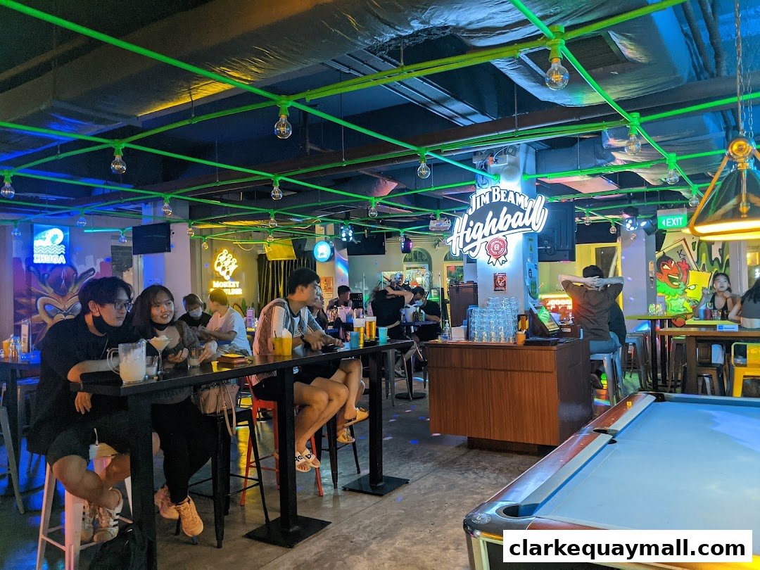People enjoying drinks and socializing at a lively arcade bar with neon lights and a pool table.