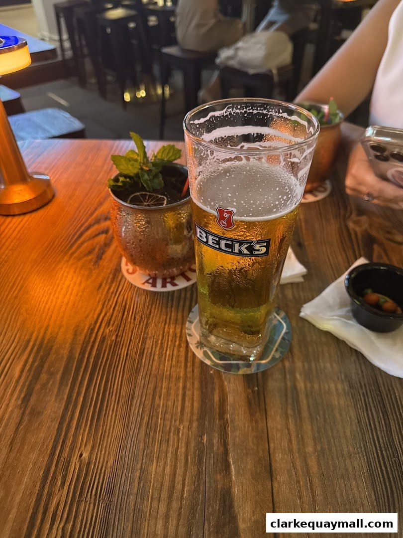 A close-up of a beer glass and a cocktail on a wooden table at a bar.