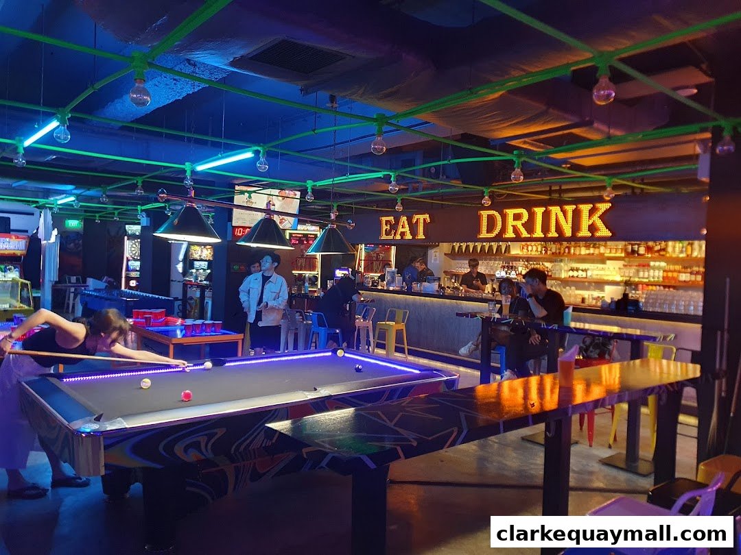 People playing pool and sitting at a bar in a neon-lit arcade bar.