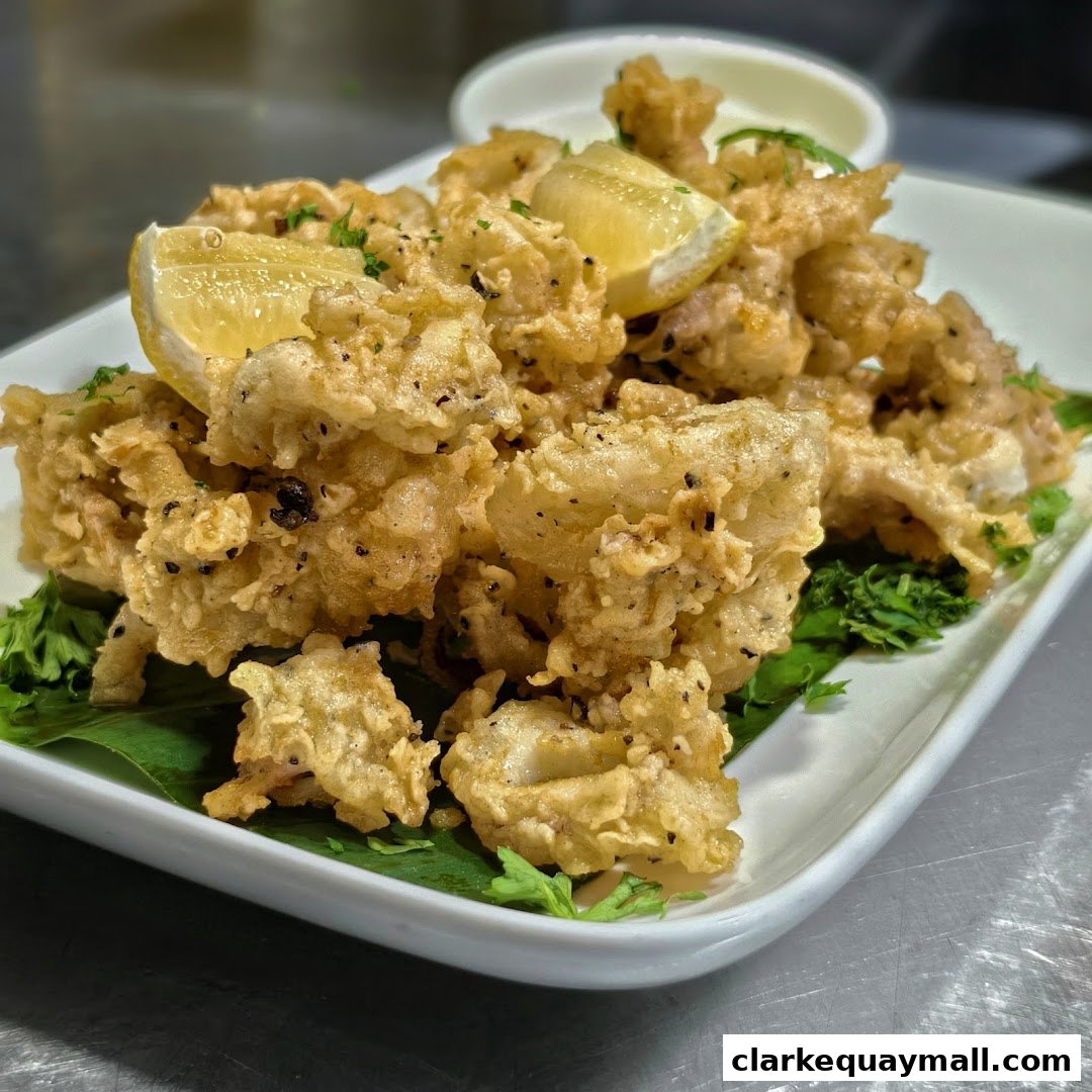 A plate of crispy fried calamari with lemon wedges and a side of dipping sauce.