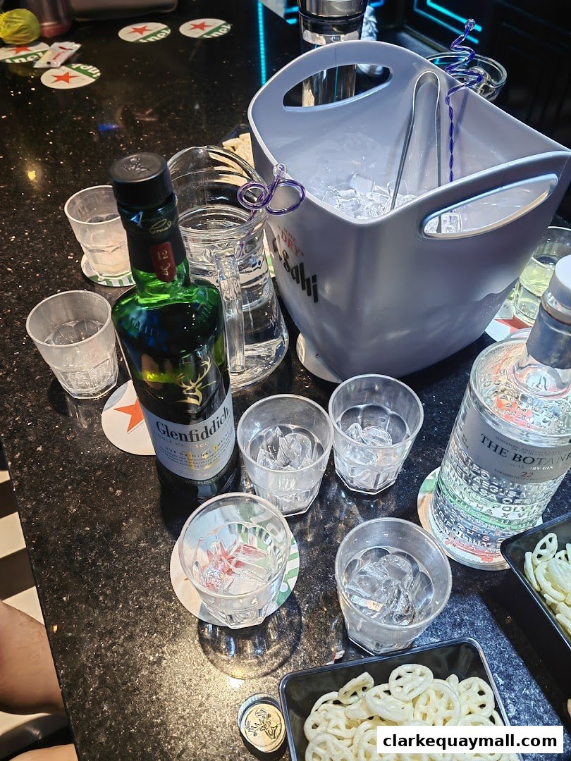 A table setting with a bottle of Glenfiddich, gin, ice bucket, glasses, and snacks.