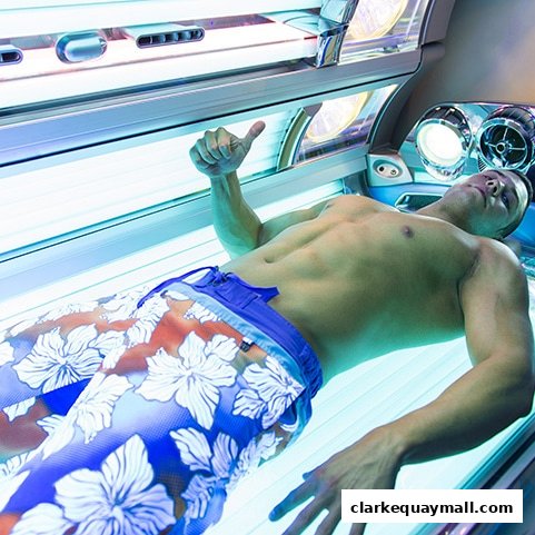 A man lies in a tanning bed, giving a thumbs up.