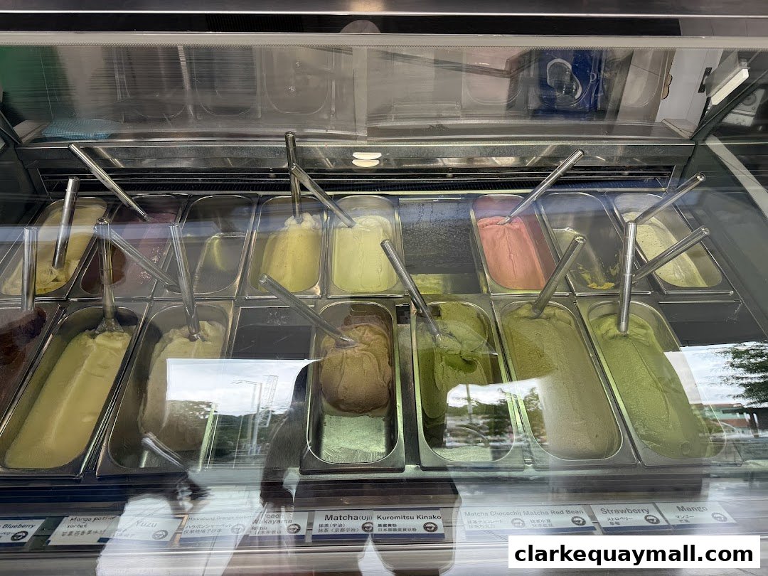 A display case filled with various flavors of gelato, including matcha and fruit flavors.