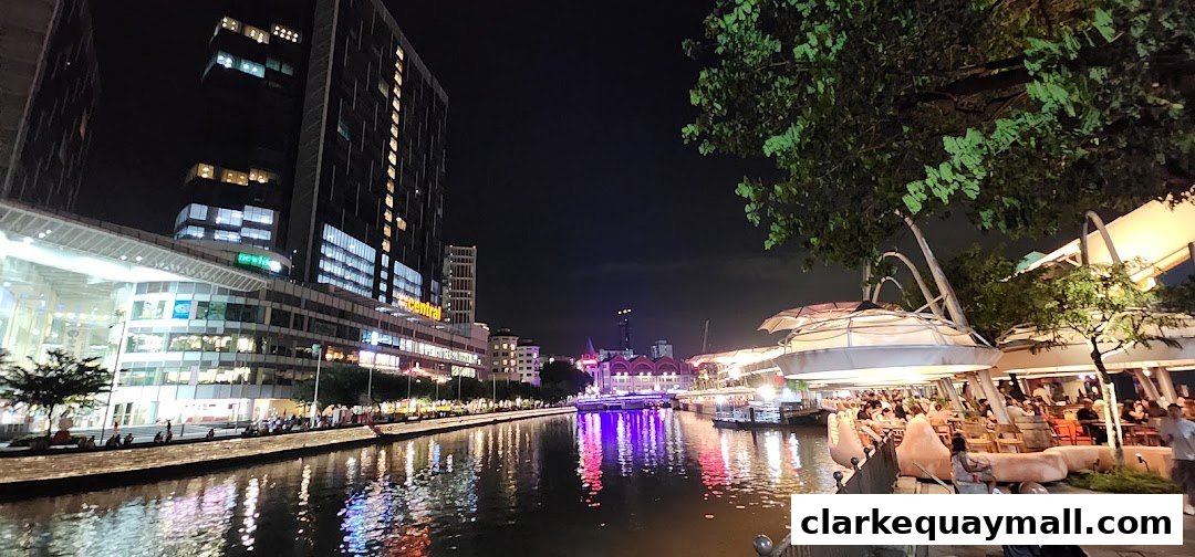 Night view of a lively riverside entertainment district with illuminated buildings and outdoor seating.