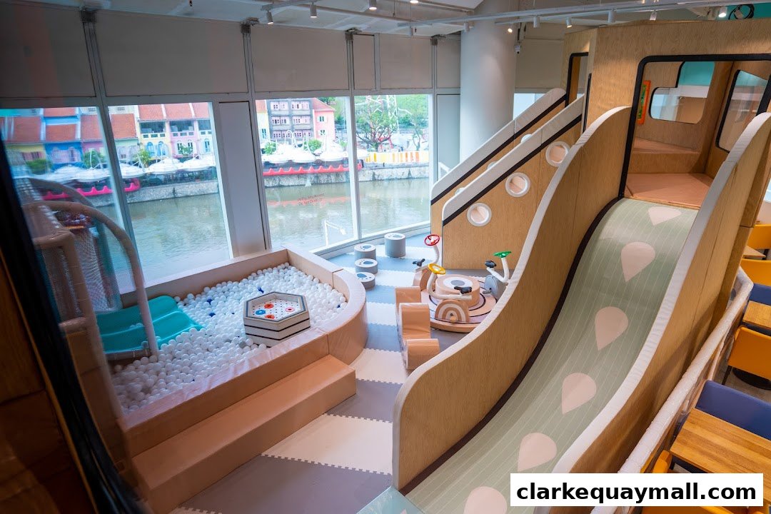A brightly lit indoor playground with a ball pit, slides, and play structures overlooking a river.