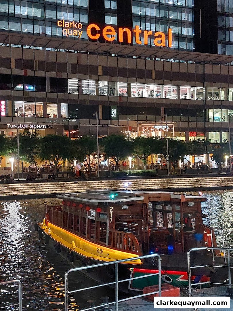 A boat docked on a river with a building labeled 'Clarke Quay Central' in the background.