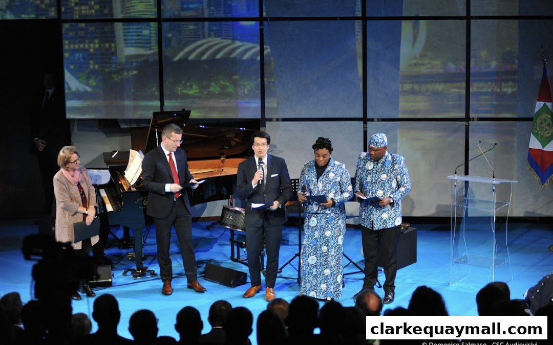 Four people on stage with a piano and a podium, in front of a city skyline backdrop.
