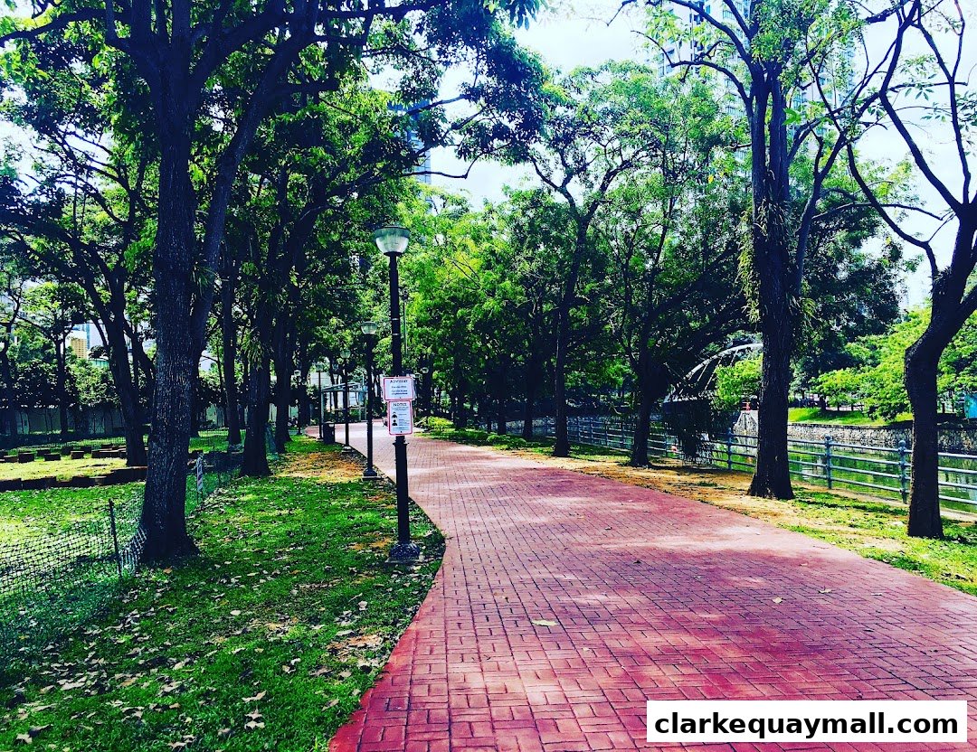 A paved pathway winds through a park with lush trees and a canal.