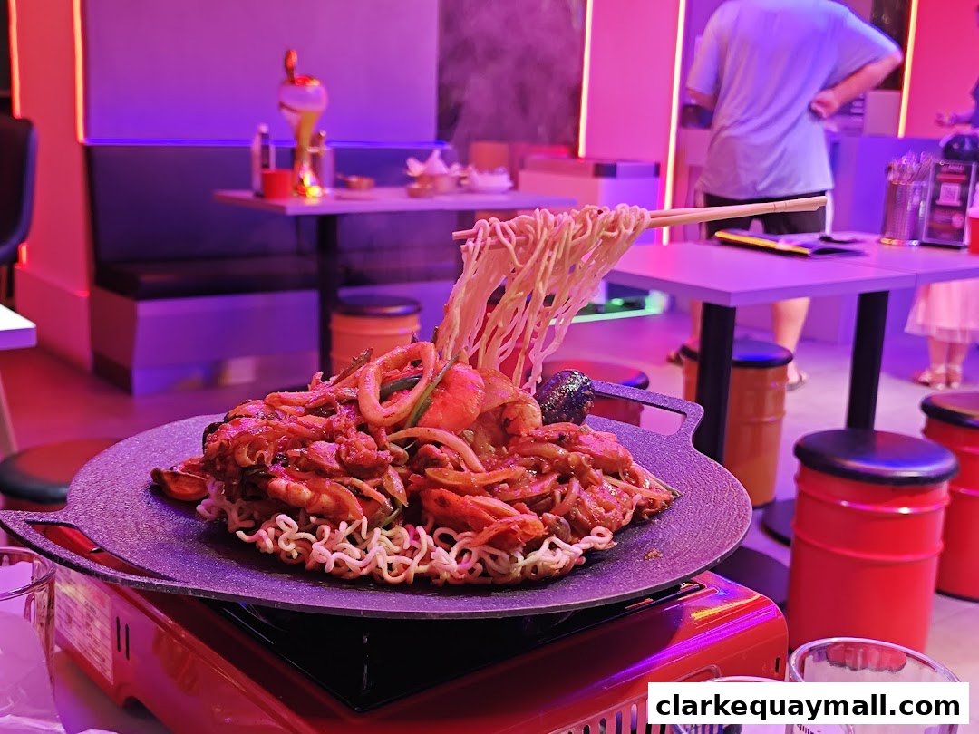 A steaming plate of Korean street food with noodles and seafood is served at a vibrant restaurant.