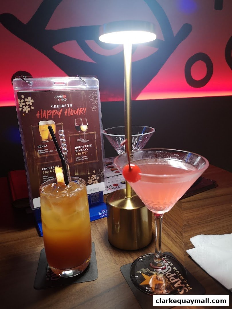 Two cocktails and a happy hour menu are displayed on a wooden table at Tomo Tokyo.