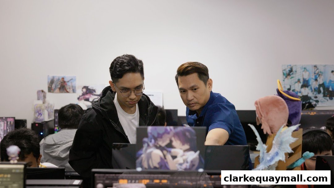 Two men are looking at a computer screen in an office with anime posters on the wall.