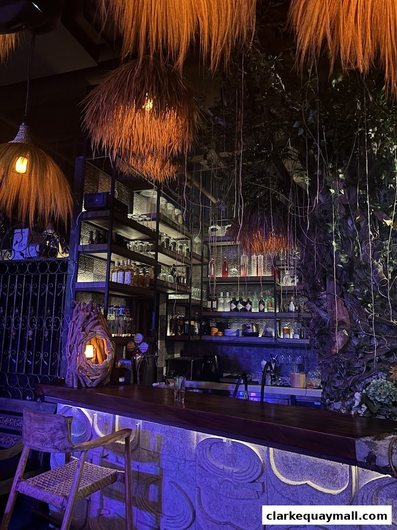 A dimly lit bar with unique straw lamps, lush greenery, and a stone-accented counter.