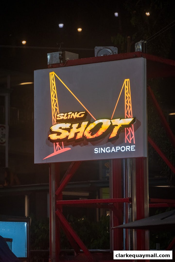 A brightly lit sign for Slingshot Singapore, featuring a bungee jumping graphic.