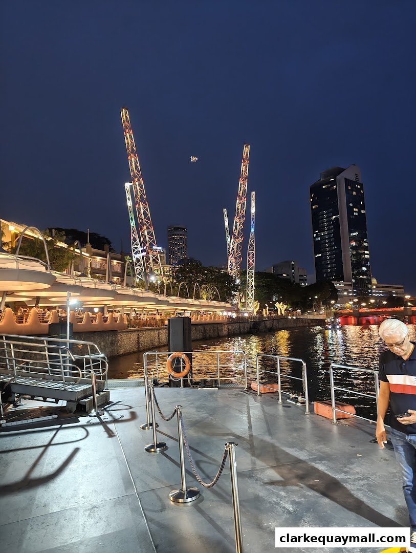 Night view of Clarke Quay with a man on a pier, illuminated towers, and a river.