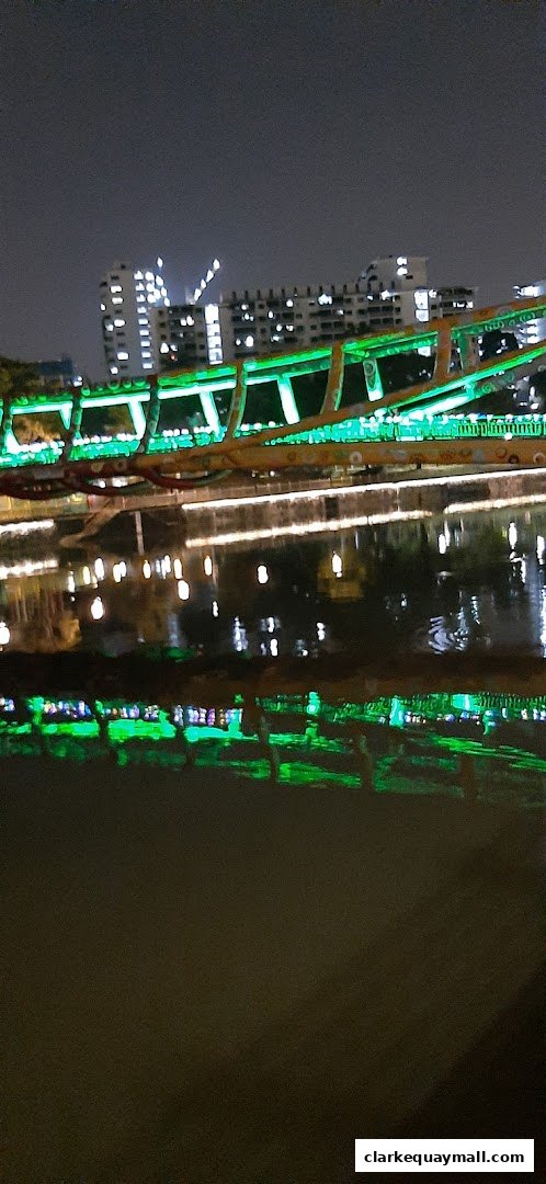 A brightly lit bridge with green lights over a dark body of water at night.