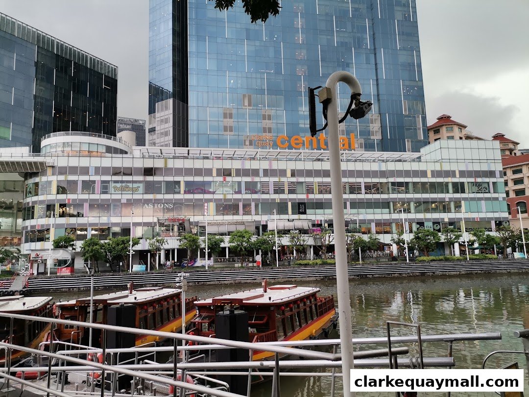 Boats docked by a river with a modern building complex in the background.