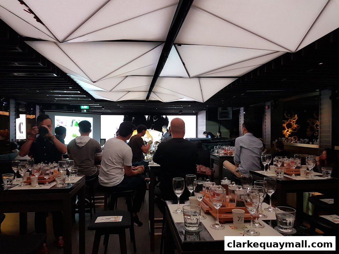 People seated at tables with glassware and tea sets in a modern, dimly lit venue.
