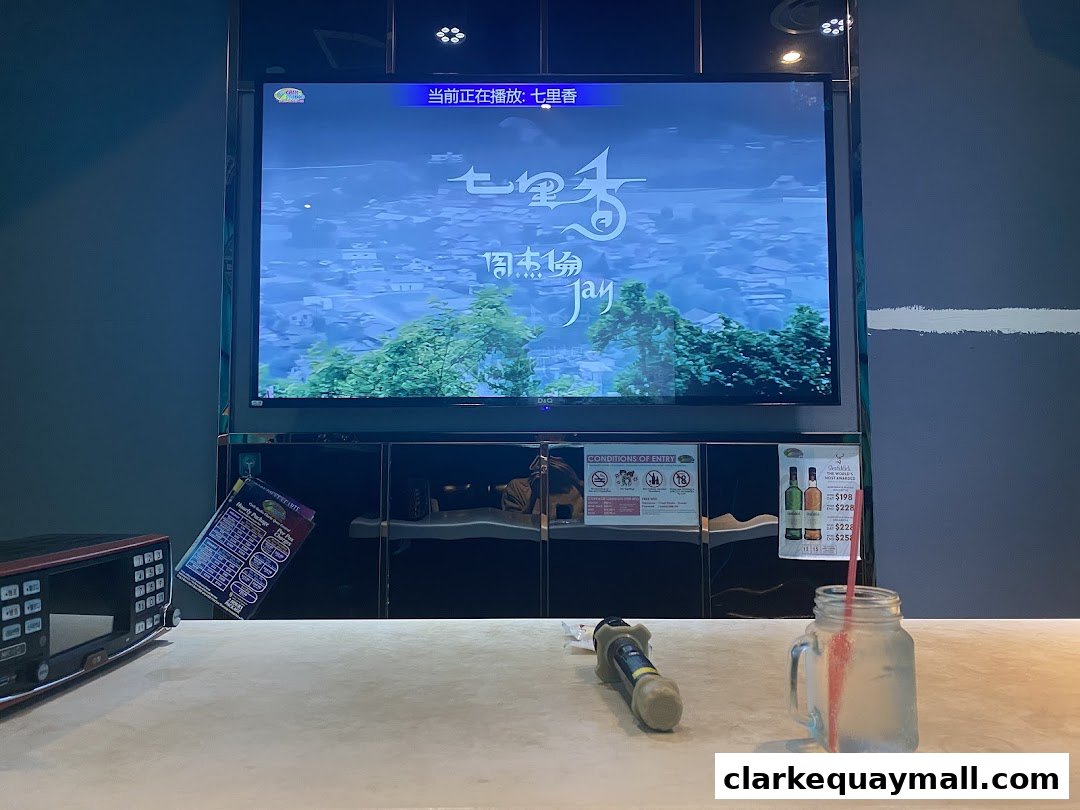 A karaoke setup with a large screen displaying lyrics, a microphone, and a drink.