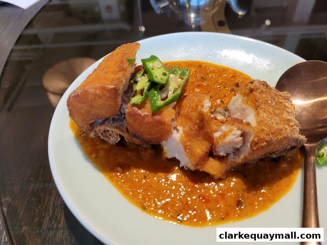 A plate of crispy fried fish with okra in a rich, orange sauce.