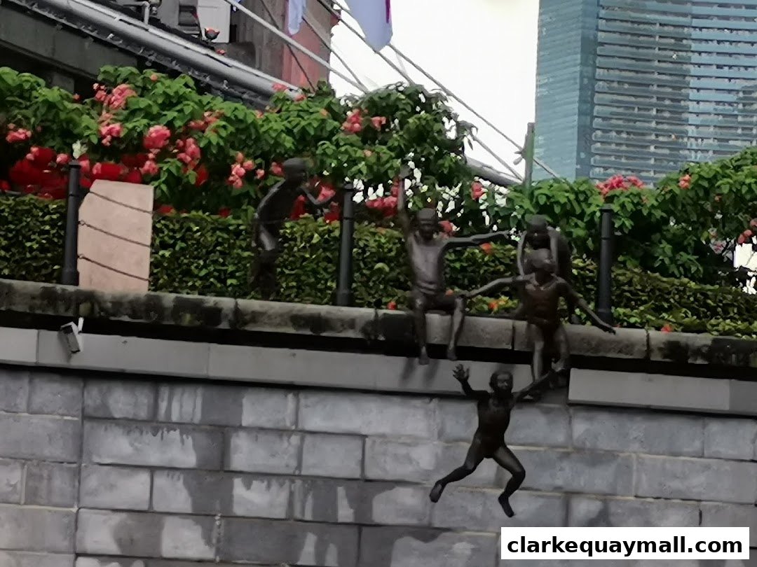 Bronze statues of children playing near a river with lush greenery and a modern skyscraper.
