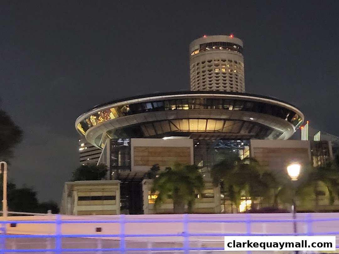 A modern building with a circular upper level and a tall tower at night.