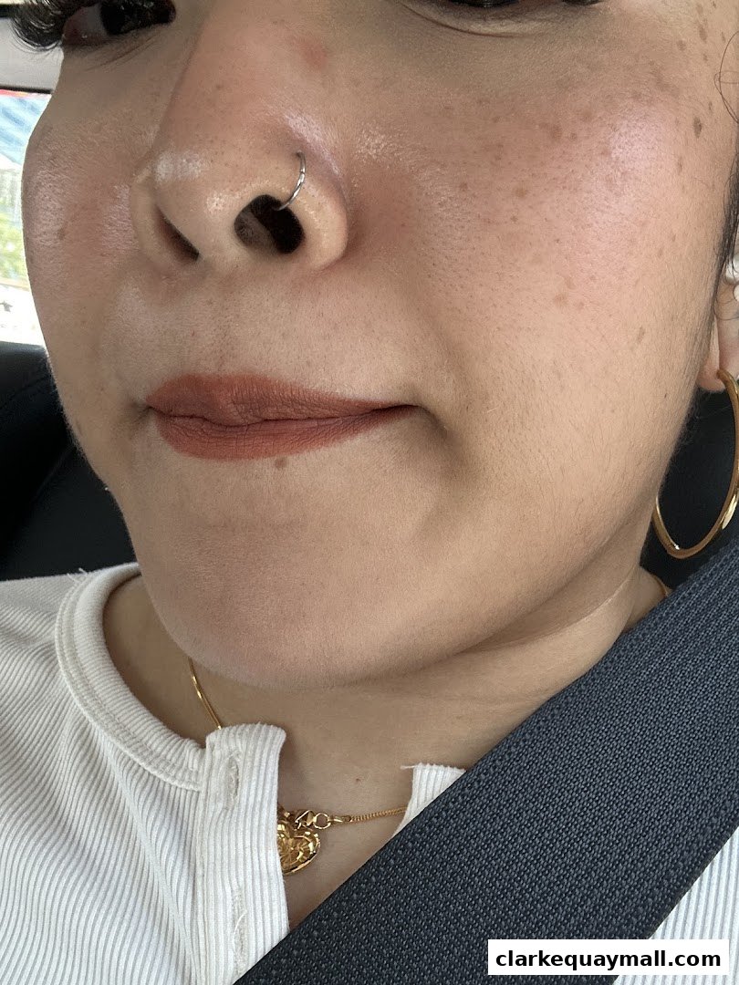 Close-up of a woman's face with nose piercing, subtle makeup, and a gold necklace.