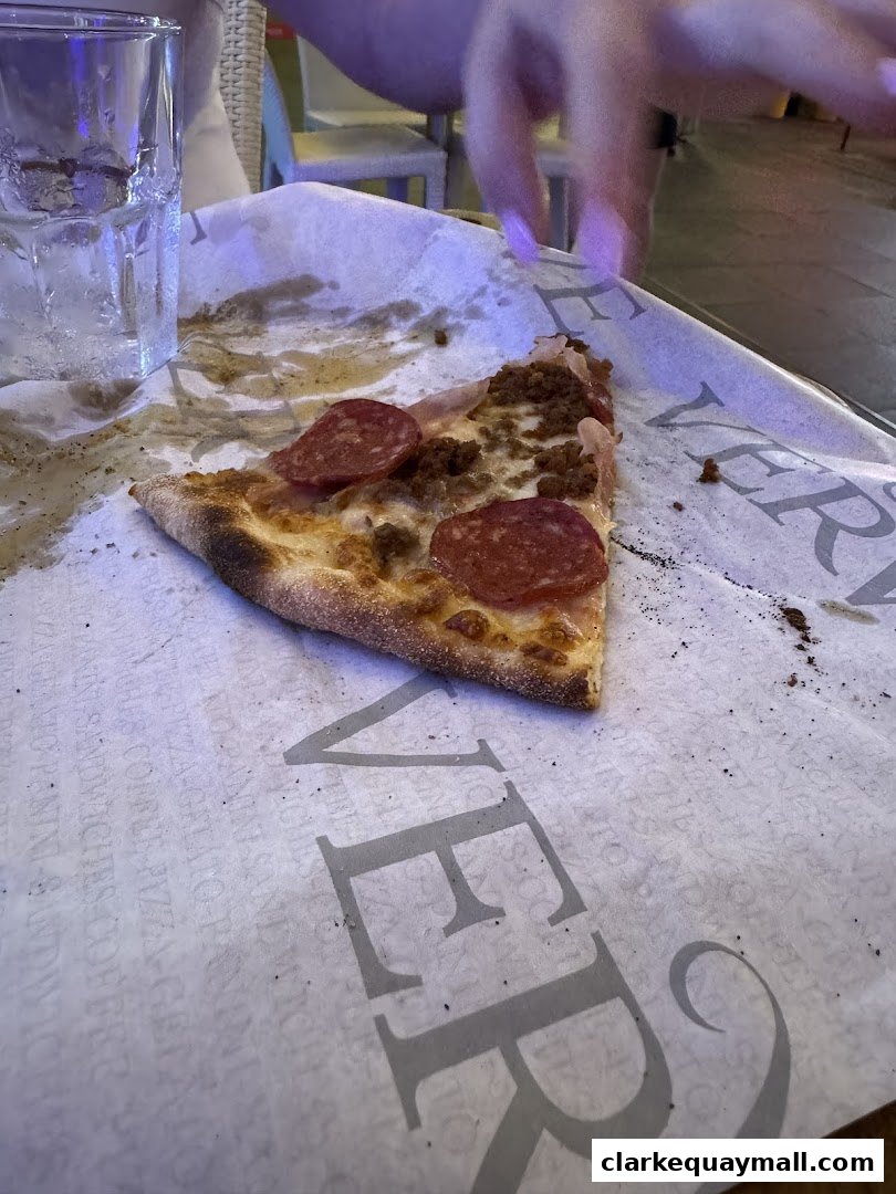 A slice of pepperoni and meat pizza on branded paper with a glass of water.