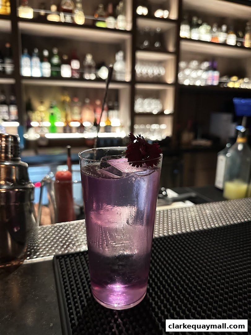 A purple cocktail with ice and a flower garnish sits on a bar counter.