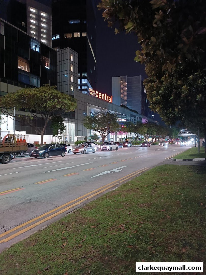 A street view at night with cars and the Clarke Quay Central building illuminated.