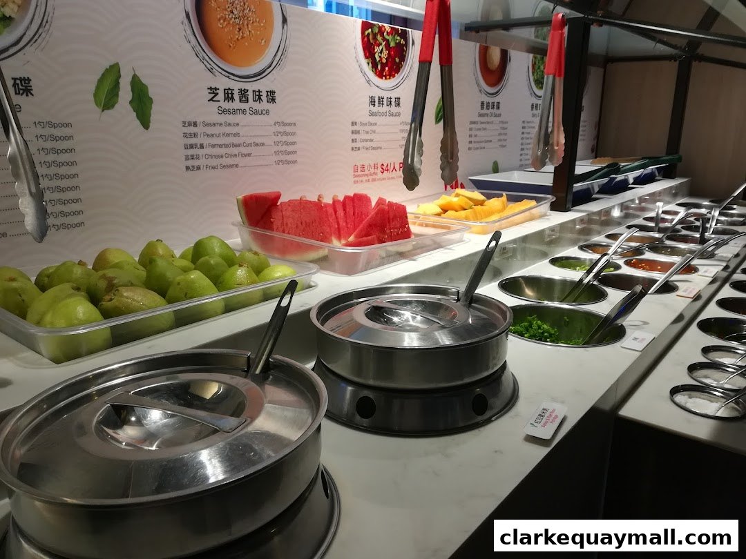 A display of fresh fruits and various dipping sauces at a hot pot restaurant.