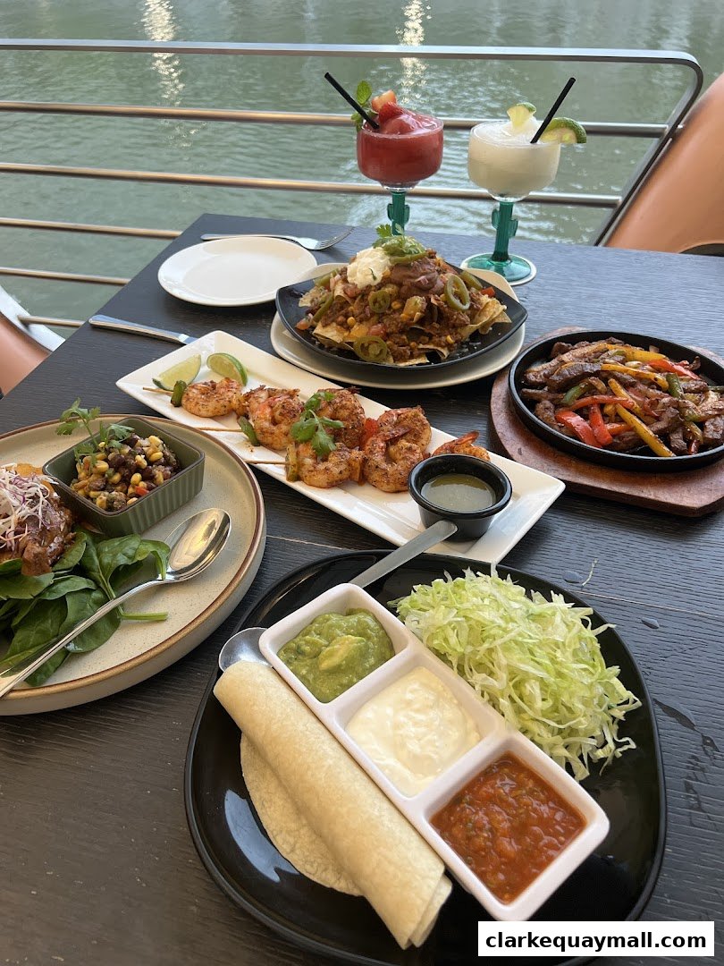 A table laden with Mexican food and colorful cocktails by the water.
