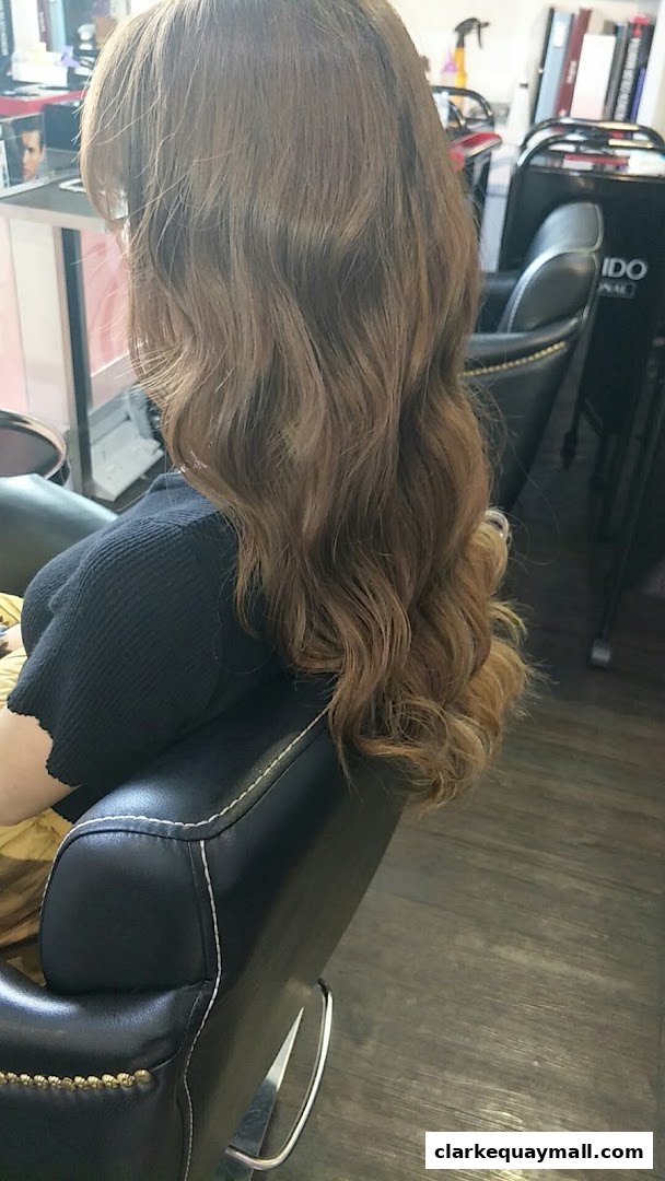 A person with long, wavy brown hair sits in a salon chair, showcasing a fresh hairstyle.