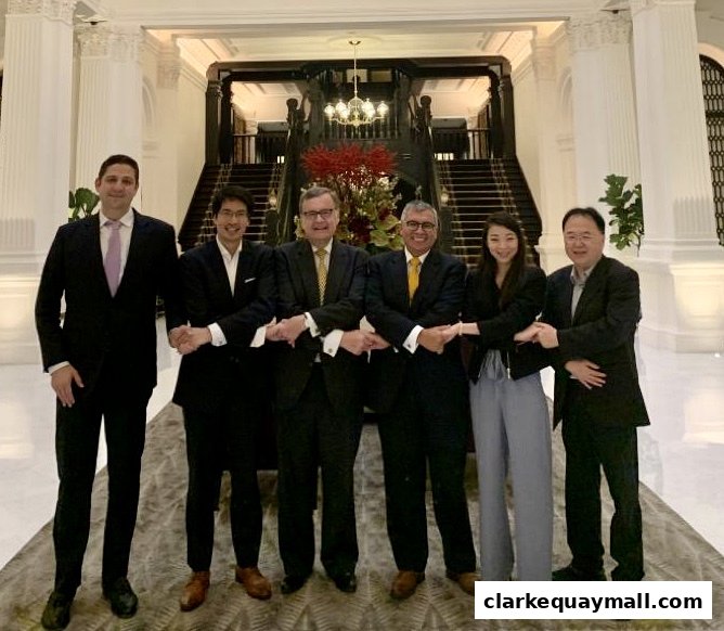 A group of six professionals in business attire holding hands in a grand lobby.
