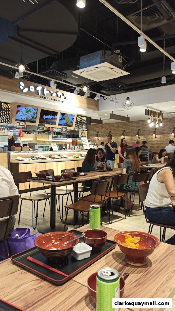 Diners enjoying meals at tables inside a Japanese restaurant with a food display counter.