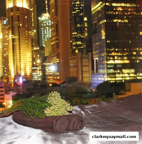Rolled towels and greenery are displayed against a backdrop of illuminated city skyscrapers at night.