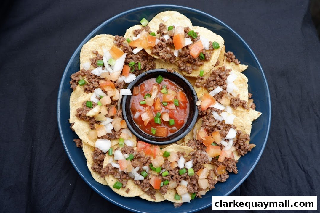 A plate of nachos topped with seasoned ground beef, diced tomatoes, and onions, served with salsa.