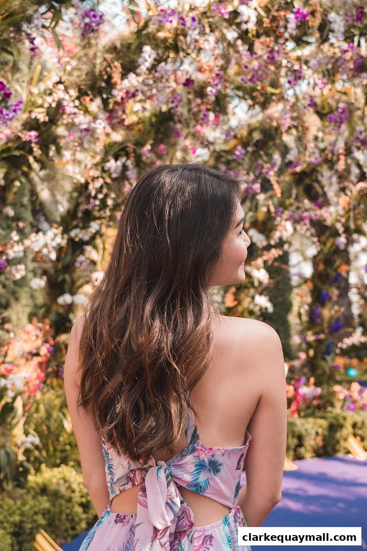 A woman with long brown hair stands in front of a vibrant floral display.