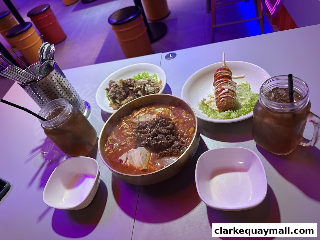 A table laden with Korean street food, including a hearty stew, a corn dog, and drinks.