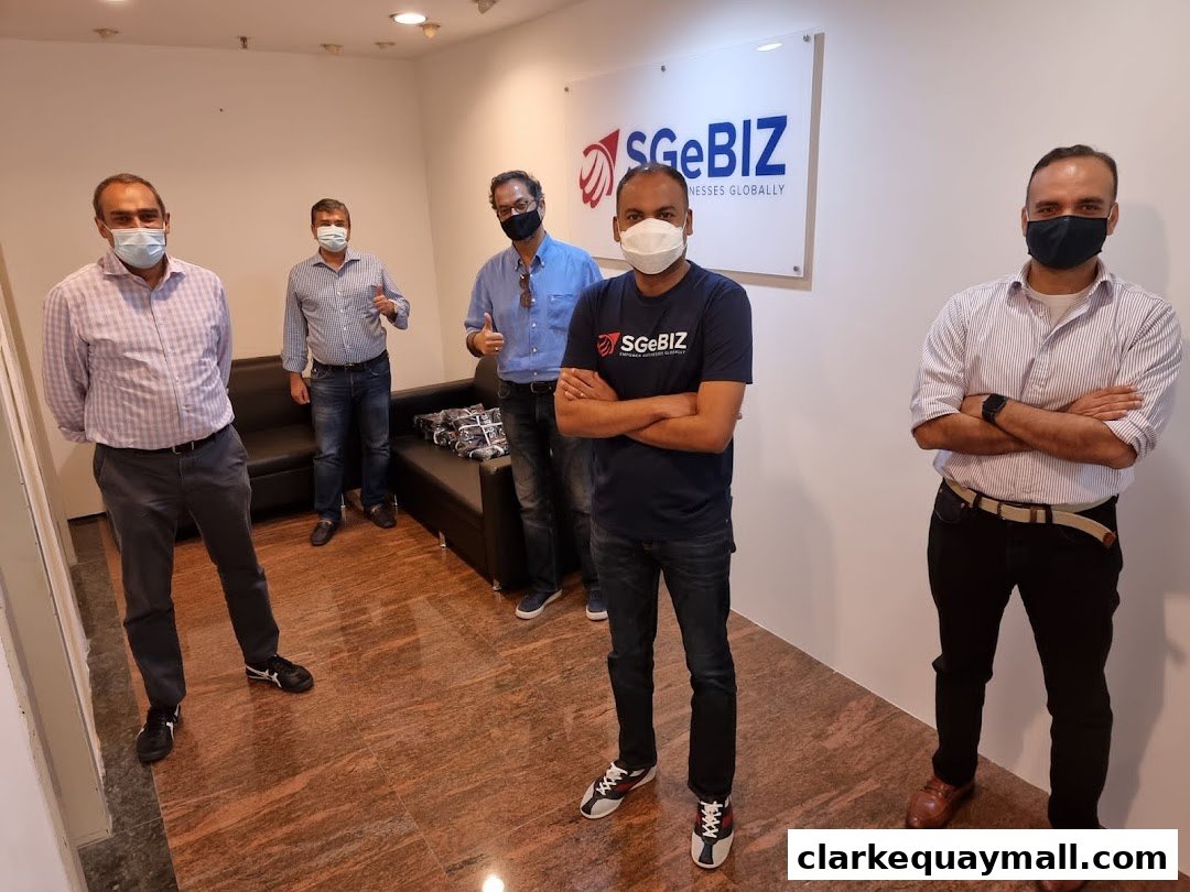 Five men in masks stand in an office with the SGeBIZ logo on the wall.