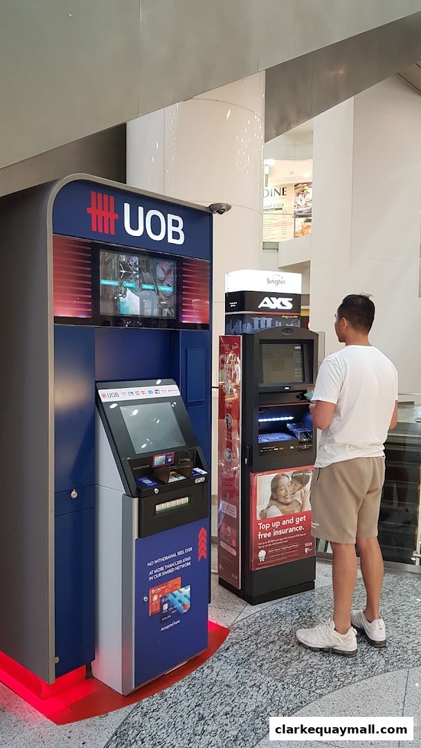 A person uses a UOB ATM machine next to an AXS machine in a shopping mall.