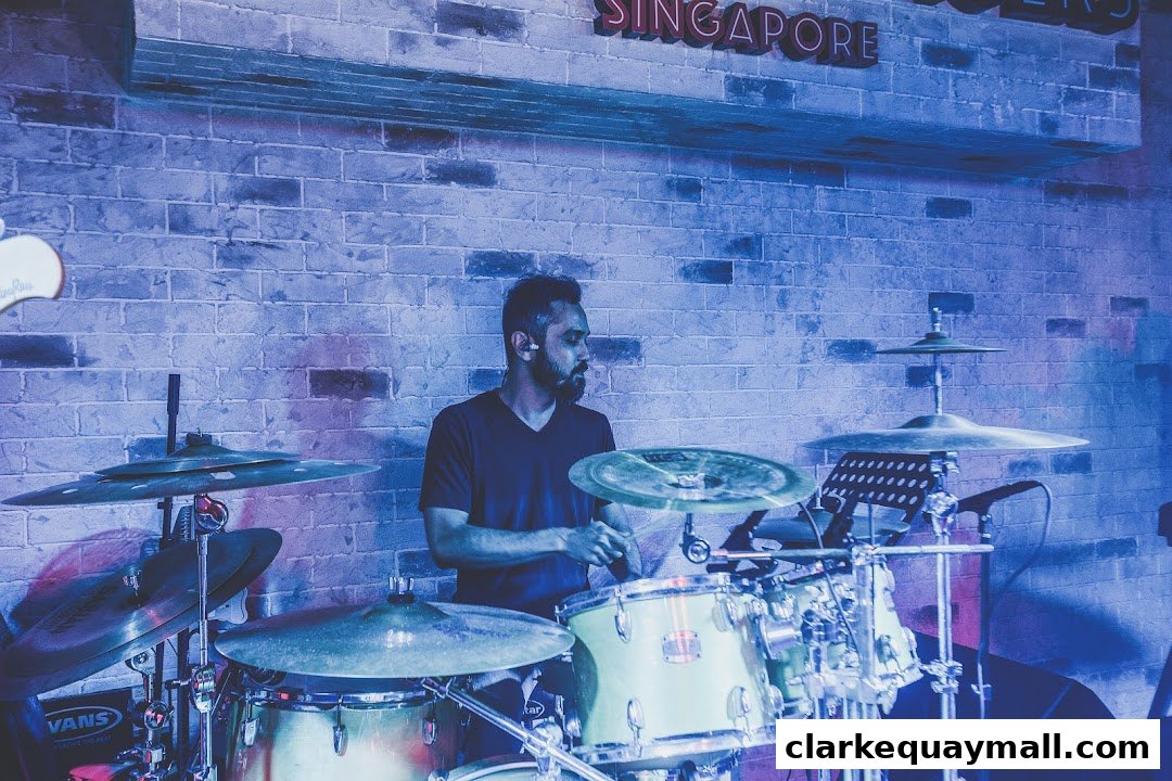 A man plays drums at a bar with a brick wall and neon sign in the background.