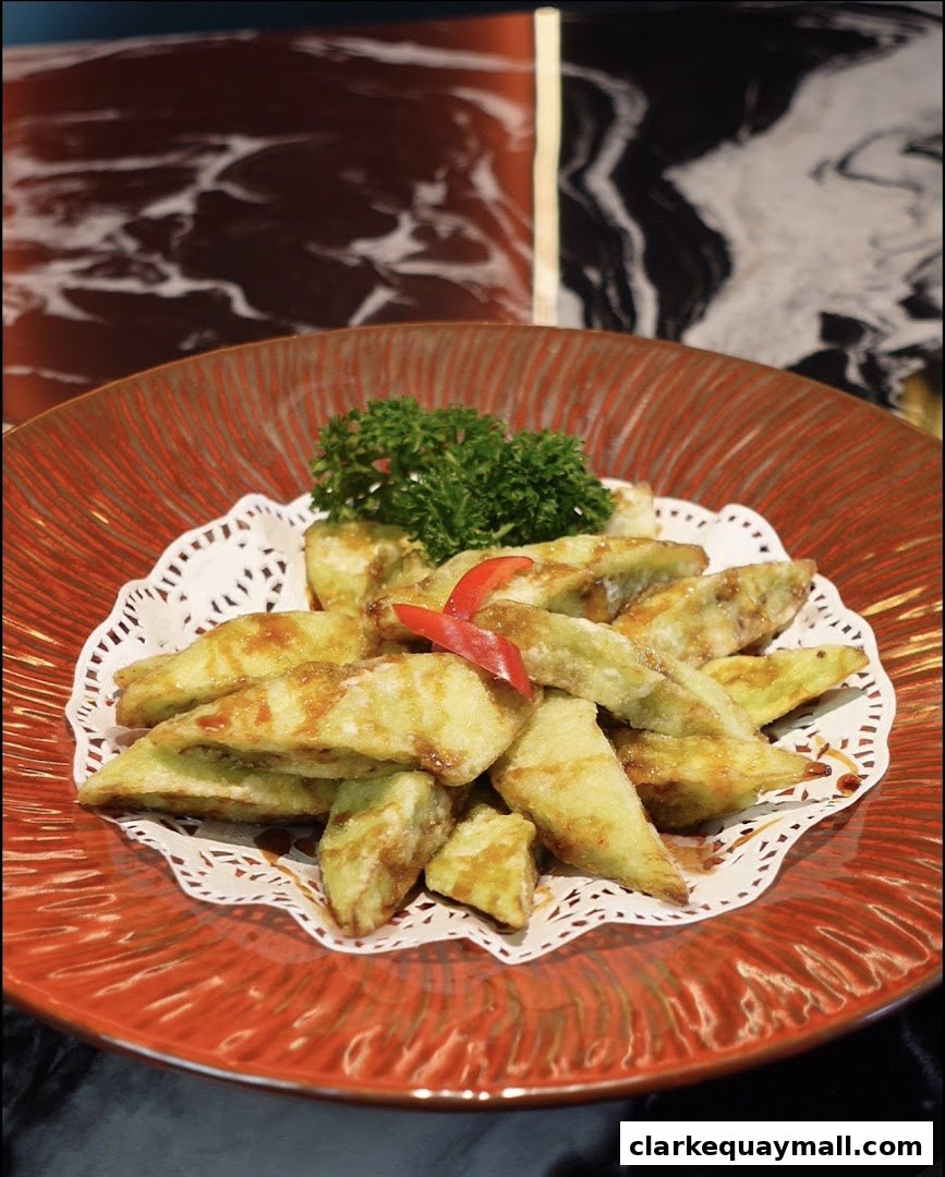A close-up of fried eggplant slices drizzled with sauce, garnished with parsley and chili.