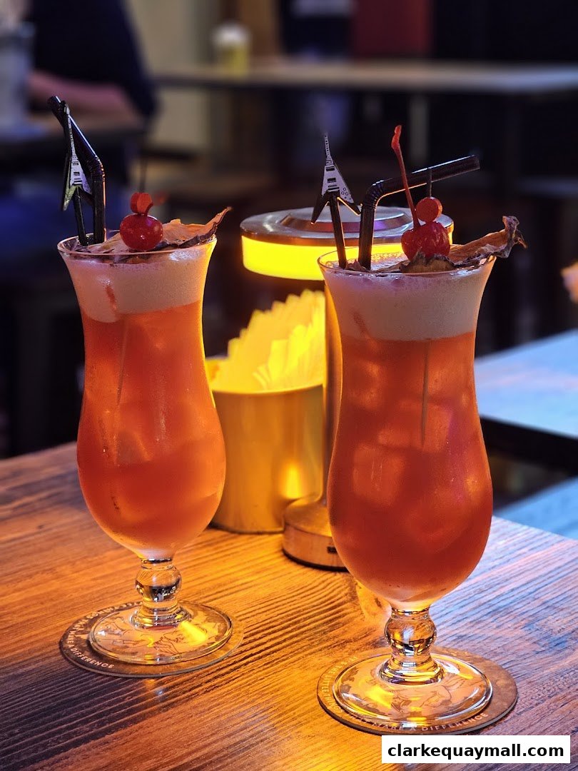 Two vibrant red cocktails with cherries and guitar-shaped stirrers on a wooden table.
