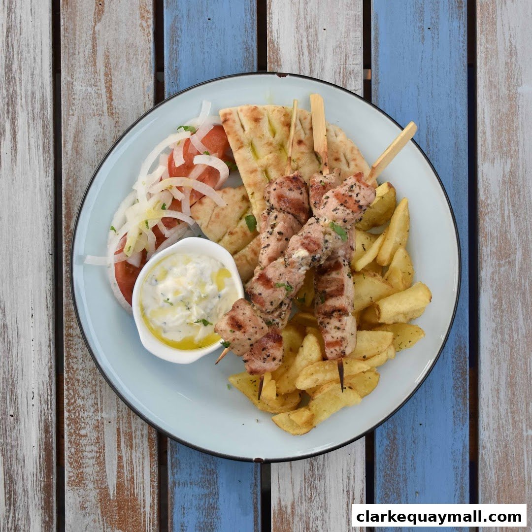 A plate of Greek souvlaki with fries, pita bread, salad, and tzatziki sauce.