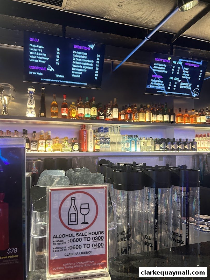 A bar counter with various bottles of alcohol and digital menus displaying drink options.