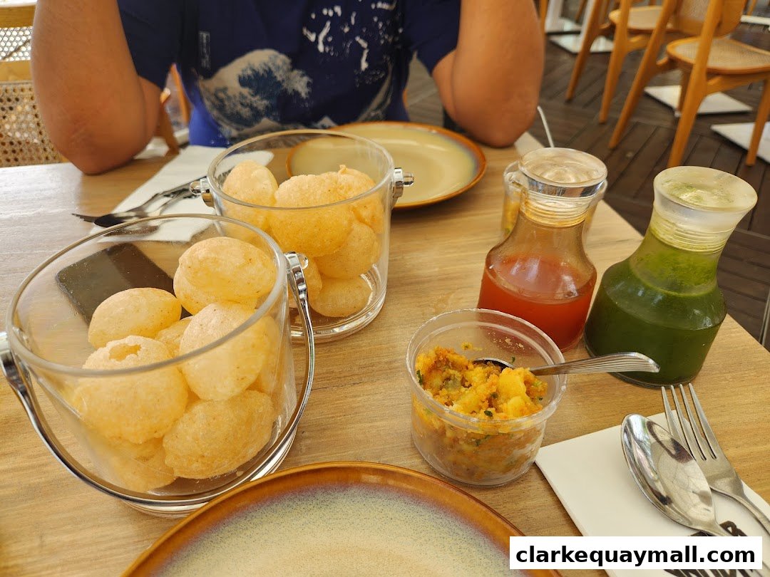 A table setting at Gabbar Bistro with pani puri, chutneys, and cutlery.